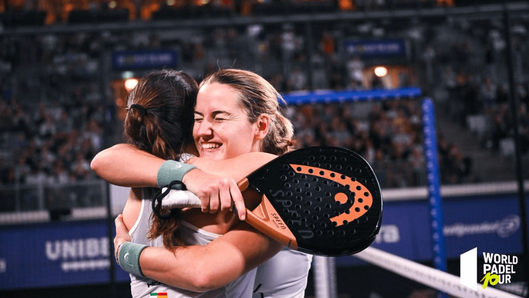 Zwei Padel-Spielerinnen umarmen sich freudig auf dem Platz, jede hält einen Schläger in der Hand. Im Hintergrund sind ein Publikum und das Logo der „World Padel Tour“ zu sehen, was eine feierliche Sportatmosphäre vermittelt und andeutet, was einen Profispieler auch nach einem spannenden Match noch glänzen lässt.