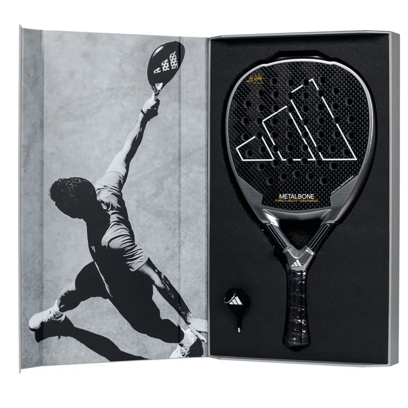Ein schwarzer Adidas Metalbone Pro EDT 2024 Padelschläger liegt in einer offenen Box, deren Deckel ein Graustufenbild eines Athleten in Aktion auf dem Padelplatz zeigt, das den Geist des Sports einfängt. Neben dem Schläger finden Sie ein praktisches Werkzeug, das Ihr Spielerlebnis verbessern soll.